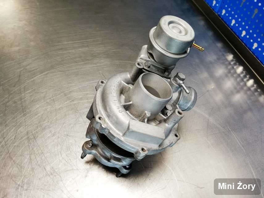 Wyczyszczona w przedsiębiorstwie w Żorach turbosprężarka do osobówki z logo Mini na stole w pracowni naprawiona przed nadaniem
